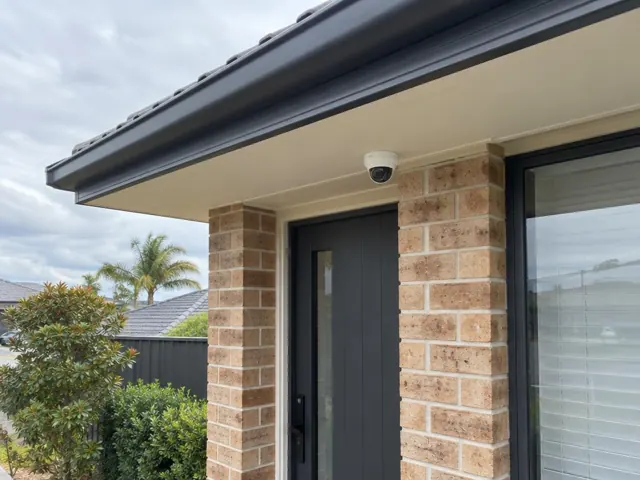 Exterior CCTV camera mounted under the eaves above a brick entry door in Southport