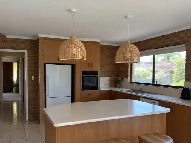 Kitchen with two woven pendant lights above an island, brick walls and timber cabinets in Parkwood